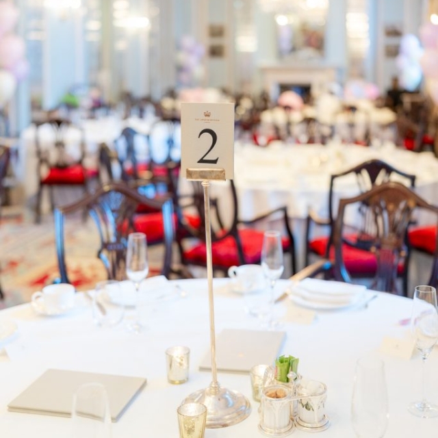 Round table set for an event with a "2" table number sign in the center, surrounded by chairs in a formal, chandelier-lit banquet hall at The Lanes.