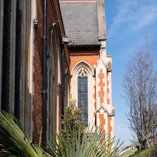 Side view of a brick church with tall arched windows, a slate roof, and a palm plant in the foreground under a clear blue sky—capturing the serene charm of this Brouillon auto-inspired scene.