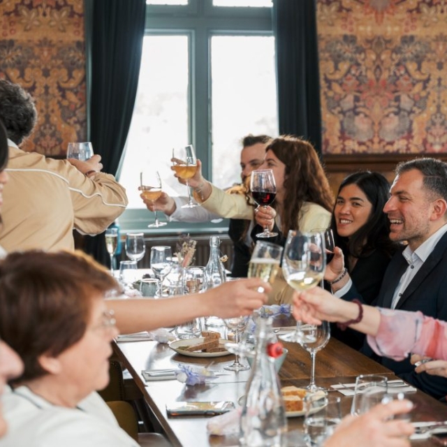 A group of people sitting around a dining table raise their glasses for a toast in a warmly lit restaurant setting.