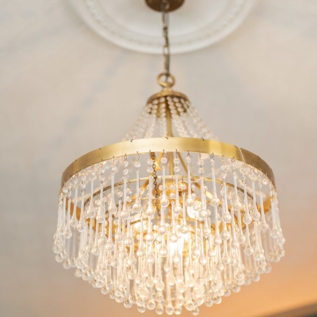 A gold and crystal chandelier hangs from a white ceiling medallion, with multiple teardrop-shaped crystals reflecting light.