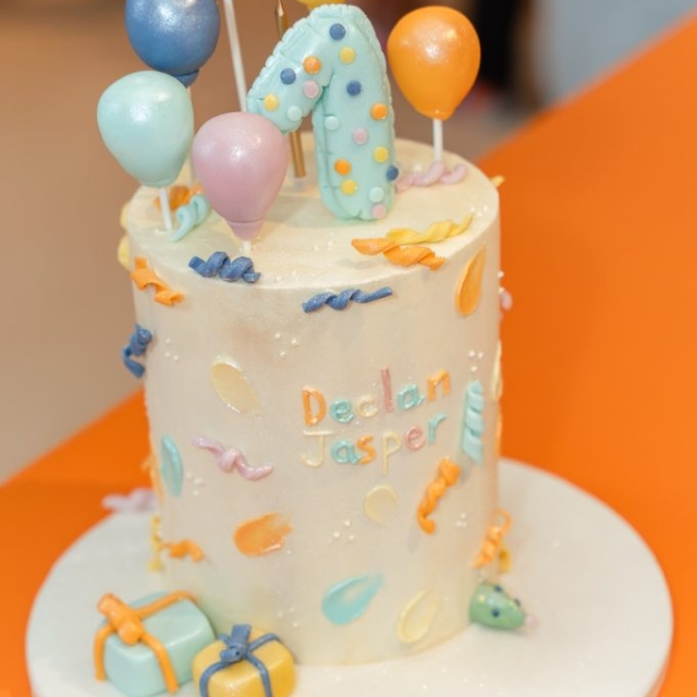 A decorated birthday cake with a large number one, colorful balloons, presents, and the name "Declan Jasper" written on it.