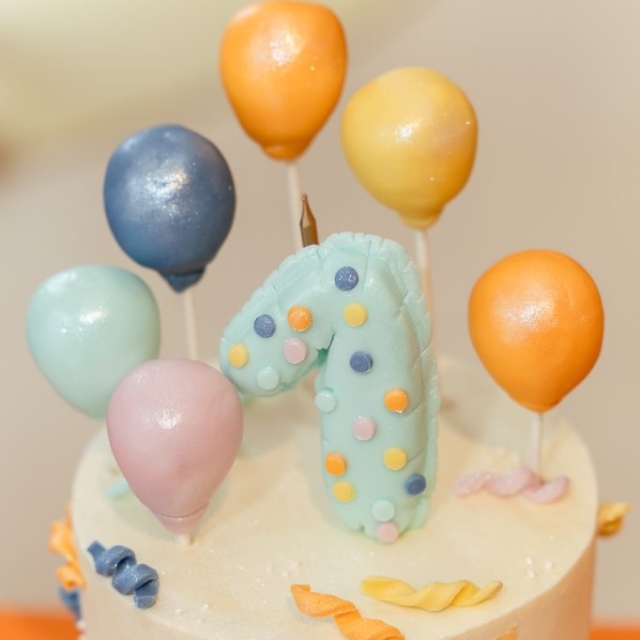 A birthday cake decorated with a large number one, colorful polka dots, and balloon-shaped cake toppers.
