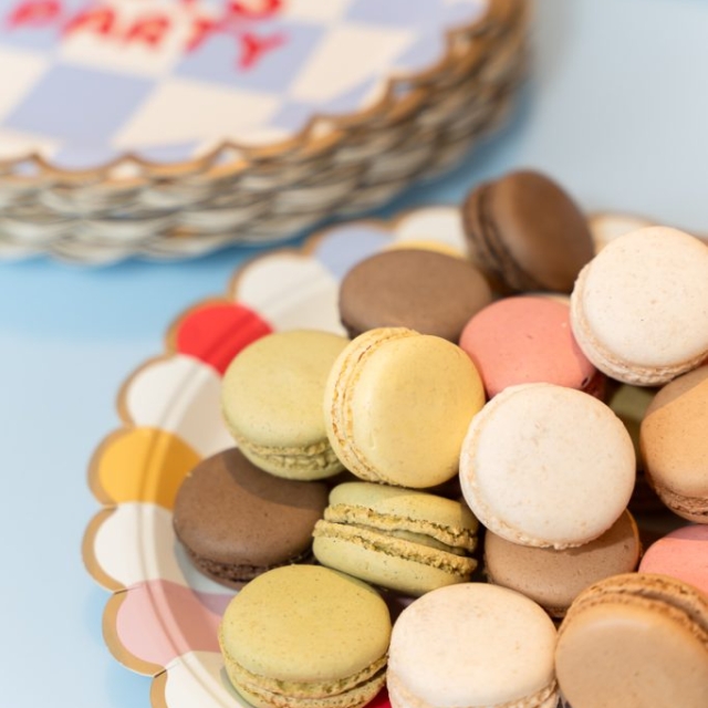 A decorative plate holds assorted macarons in pastel colors, with a stack of party-themed plates labeled "LET'S PARTY" in the background.