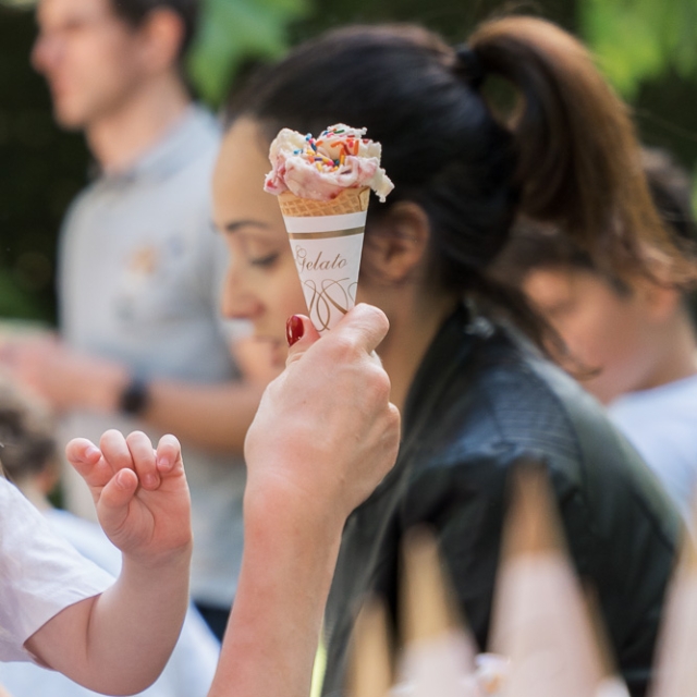 Belgravia-birthday party -photographer (12) A hand holds up an ice cream cone with sprinkles; blurred people and greenery are in the background.