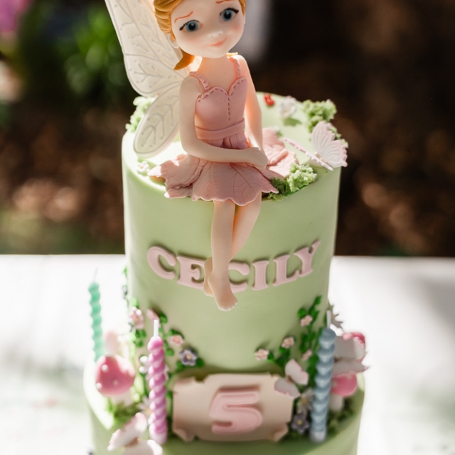 Belgravia-birthday party -photographer (14) Two-tiered green birthday cake with a fairy figurine topper, pink and white decorations, the name “CECILY,” and a “5” plaque on the front, with candles around the base.