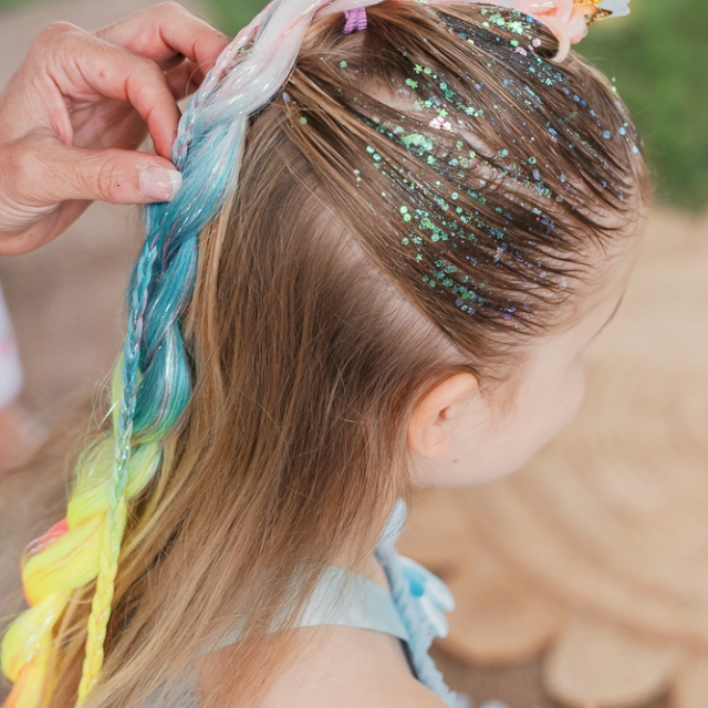 Belgravia-birthday party -photographer (7) A child with glitter on their hair is having their long, colorful braid adjusted by an adult’s hand.