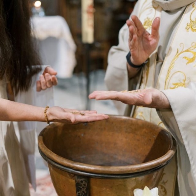 Christening-photographer-London1 A person in religious attire sprinkles water onto another person’s hand over a large copper basin, likely during an Italian battesimo, or baptism ceremony.