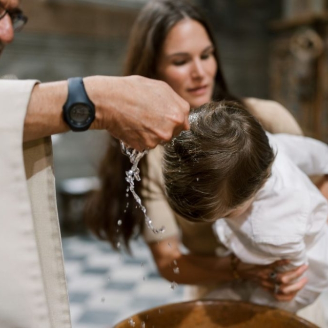 Christening-photographer-London3 A priest pours water on a child’s head during a baptism ceremony, while a woman holds the child over a basin, marking the sacred moment of baptism in English tradition.
